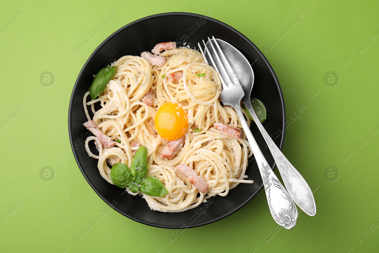 Photo of Delicious pasta Carbonara with egg yolk and cutlery on light green background, top view