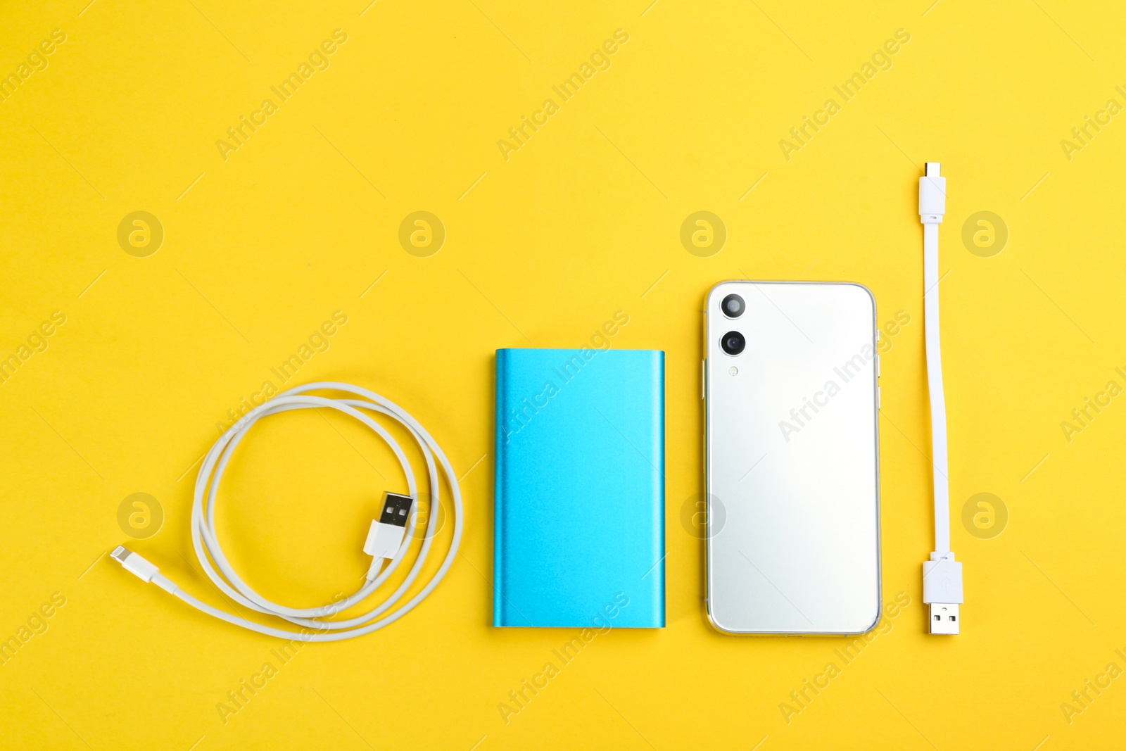 Photo of Mobile phone, portable charger and cables on yellow background, flat lay
