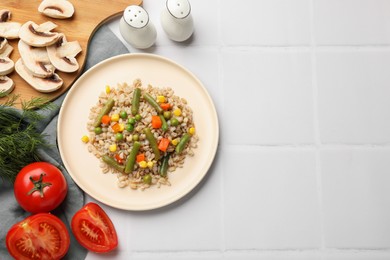 Photo of Delicious pearl barley with vegetables served on white tiled table, flat lay. Space for text