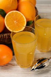 Many ripe juicy oranges, squeezer and fresh juice on white wooden table