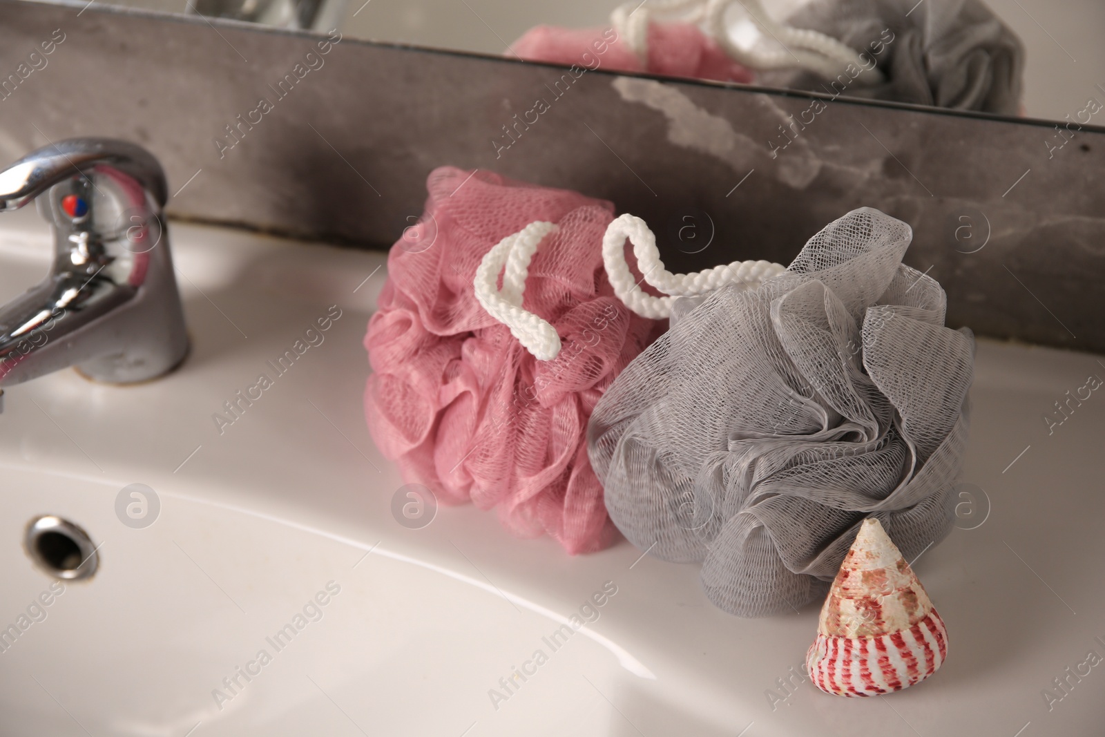 Photo of Colorful shower puffs and seashell on sink in bathroom