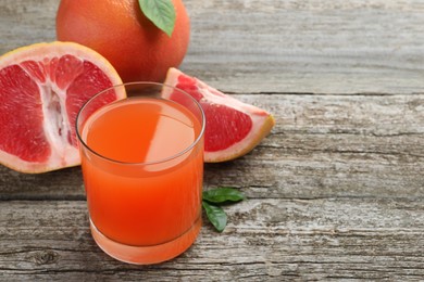 Photo of Tasty freshly made grapefruit juice and fruits on wooden table. Space for text