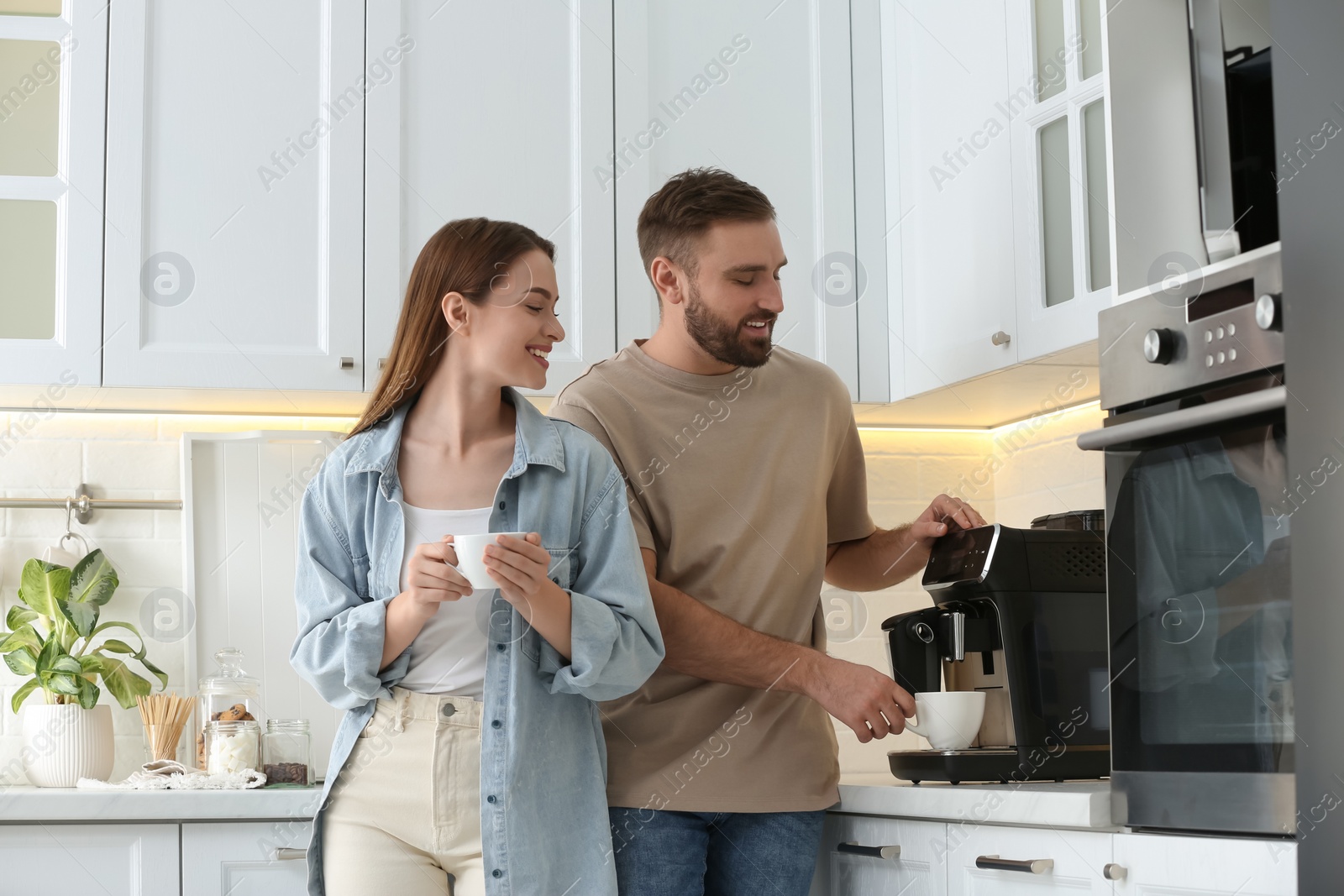 Photo of Happy couple preparing fresh aromatic coffee with modern machine in kitchen