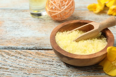 Photo of Yellow sea salt in bowl, scoop and flower on wooden table, closeup. Space for text