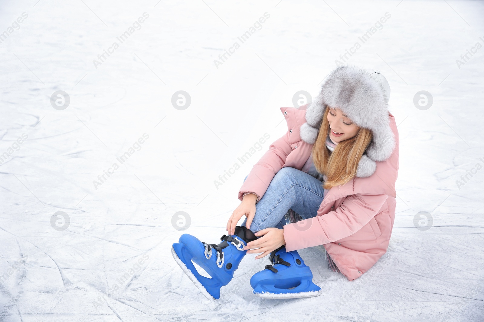 Photo of Woman adjusting figure skate while sitting on ice rink. Space for text