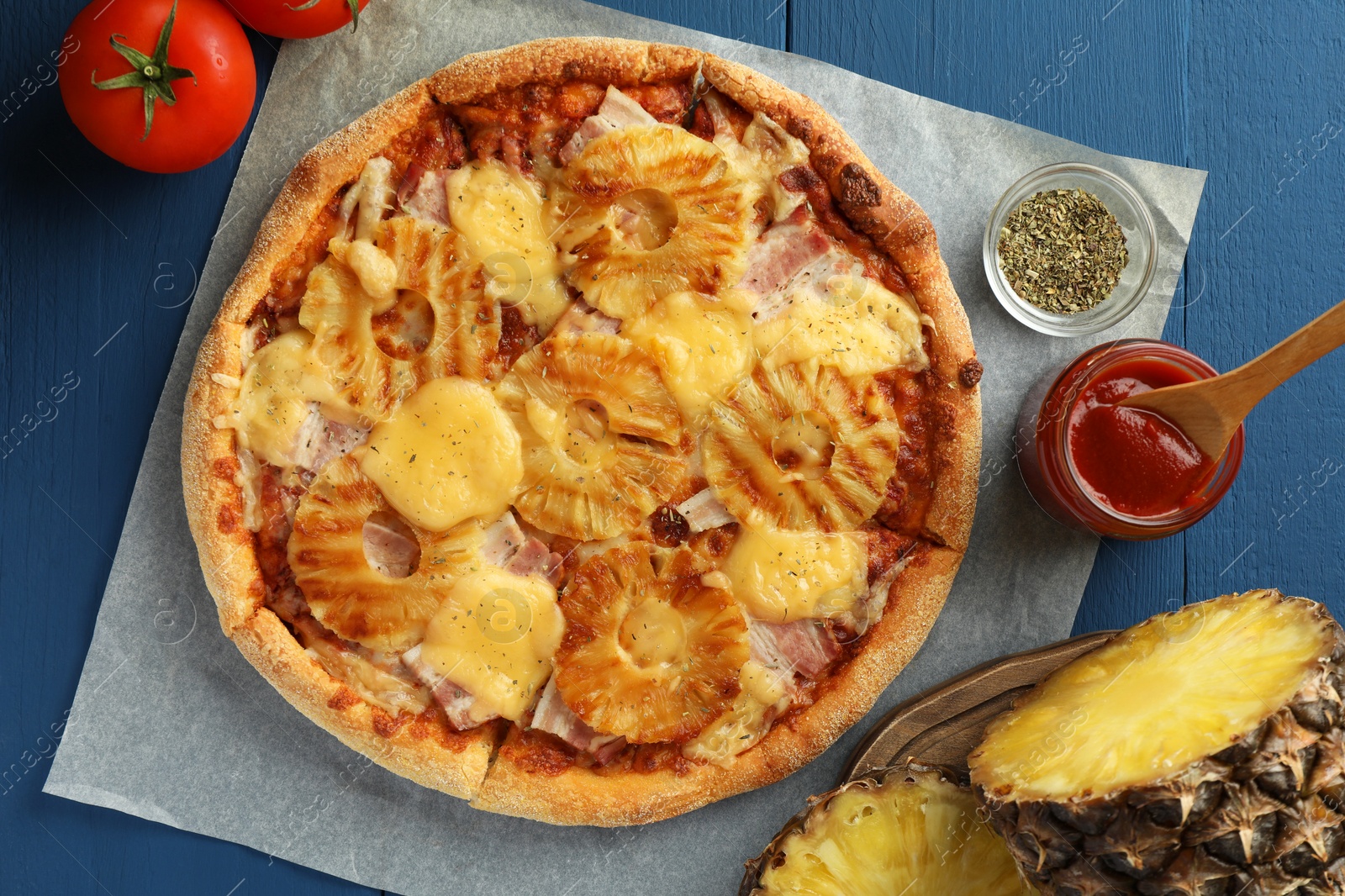 Photo of Delicious pineapple pizza and ingredients on blue wooden table, flat lay
