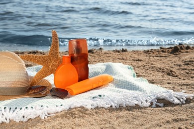 Sun protection products and beach accessories on blanket near sea, space for text