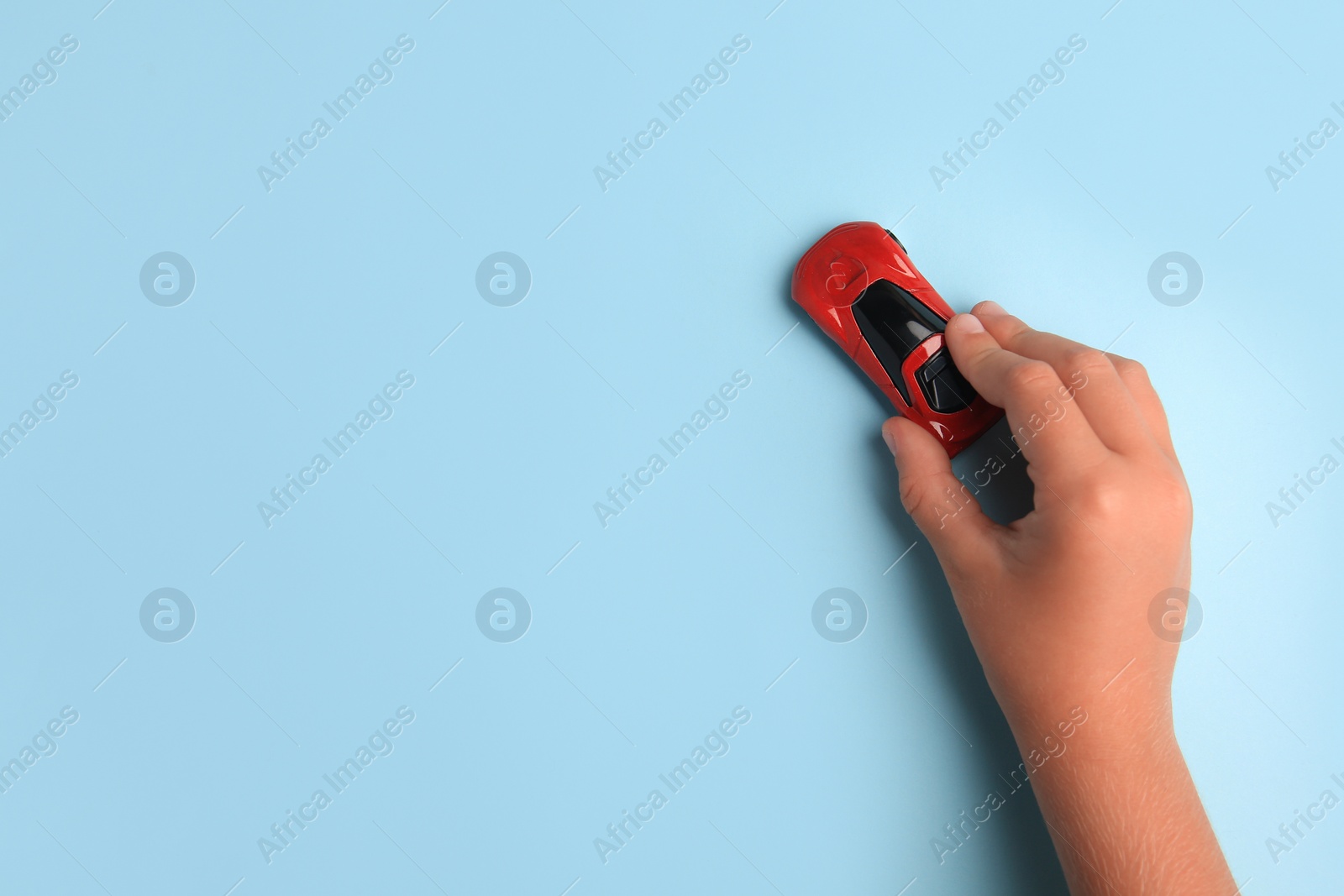 Photo of Child playing with toy car on light blue background, top view. Space for text