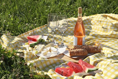 Picnic blanket with delicious food and wine on green grass outdoors