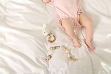 Photo of Cute baby with rattle and teether toys on sheets, top view. Space for text