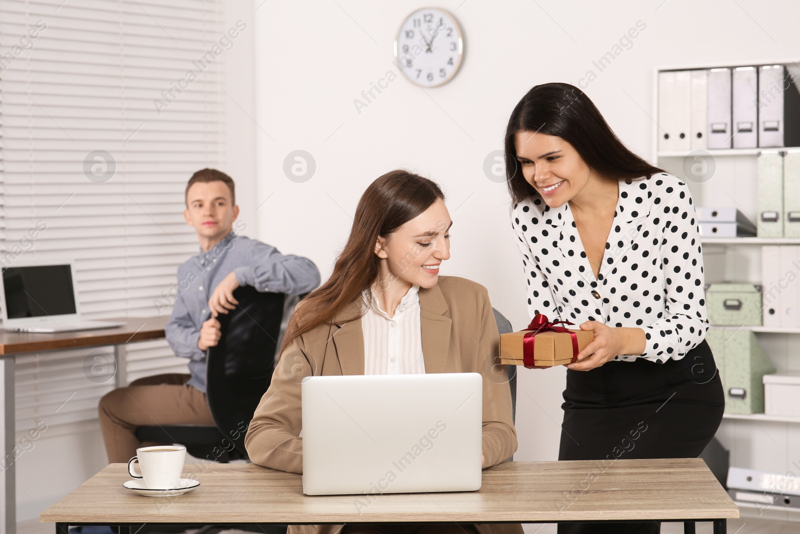 Photo of Woman presenting gift to her colleague in office