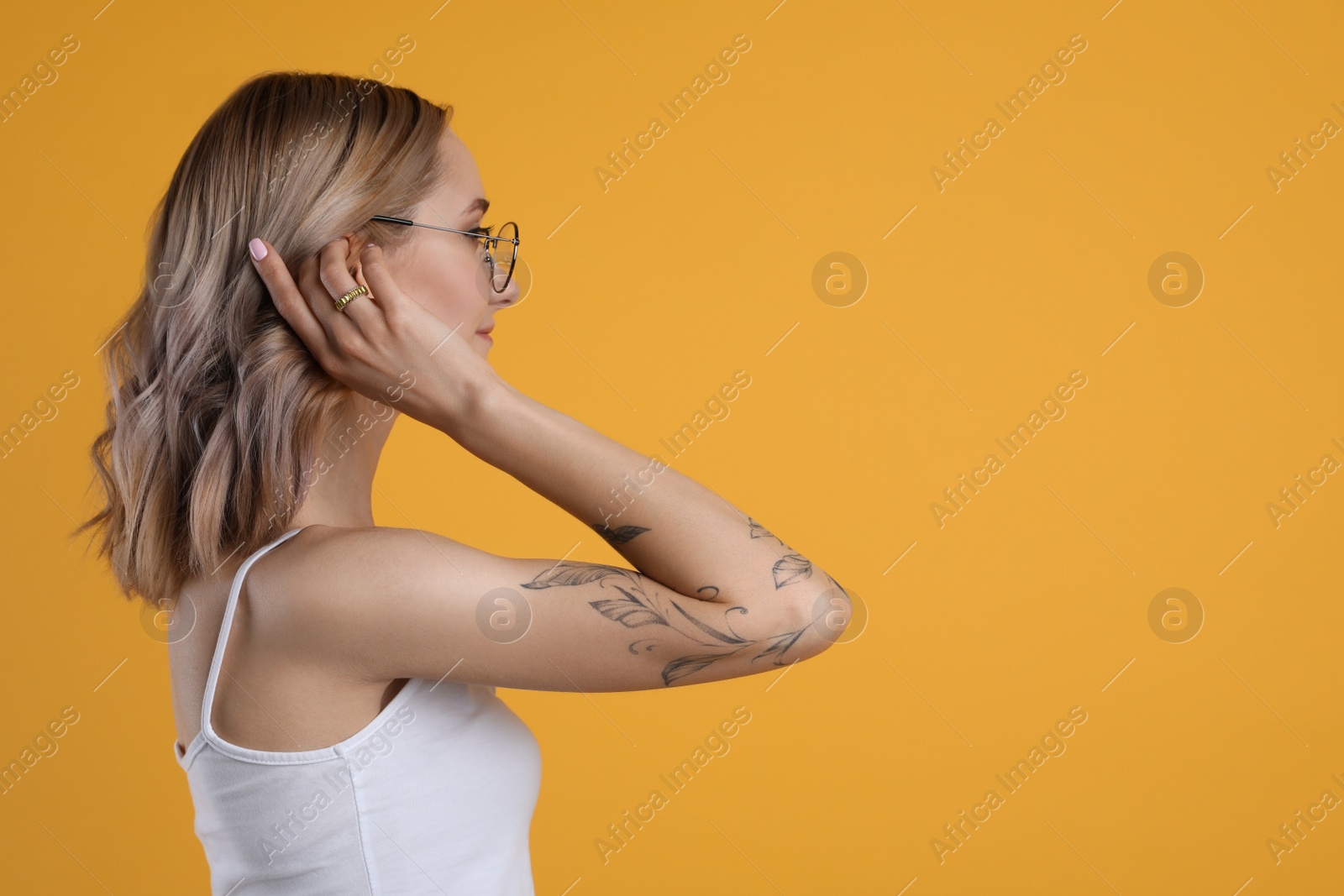 Photo of Beautiful woman with tattoos on arm against yellow background. Space for text