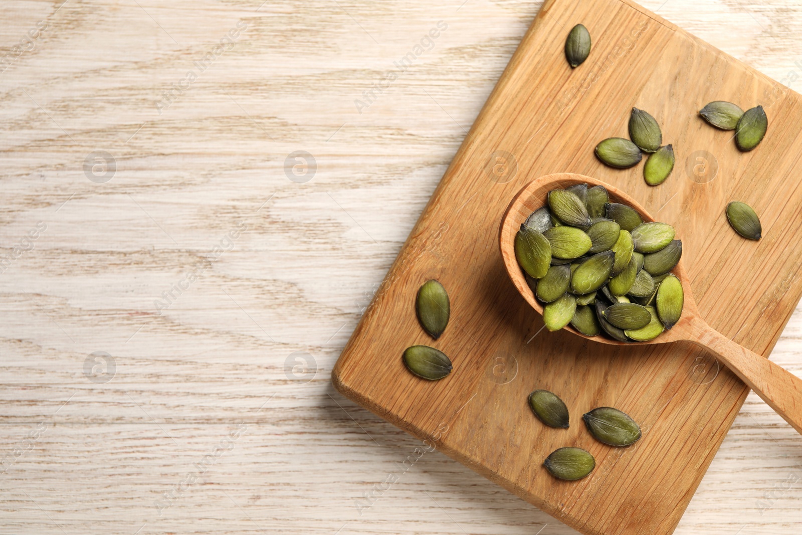 Photo of Spoon with pumpkin seeds on wooden table, top view. Space for text