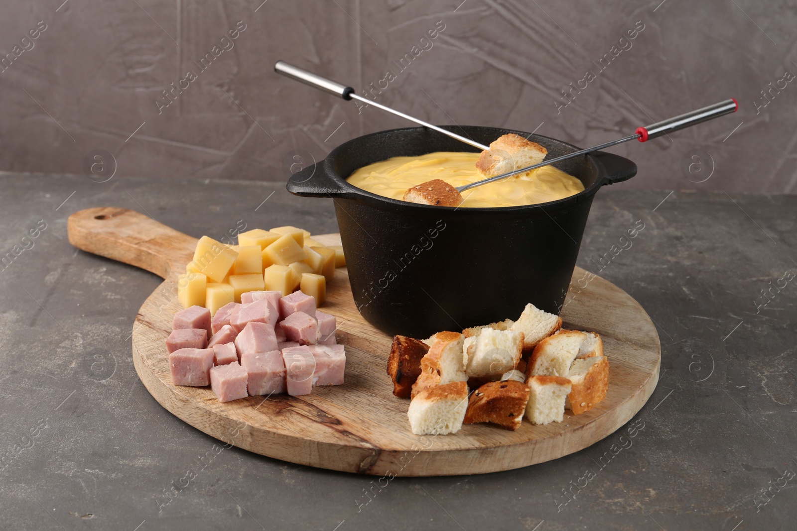 Photo of Fondue pot with tasty melted cheese, forks and different snacks on grey table