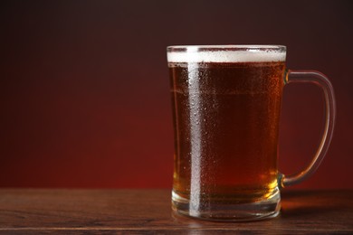 Mug with fresh beer on wooden table against color background. Space for text