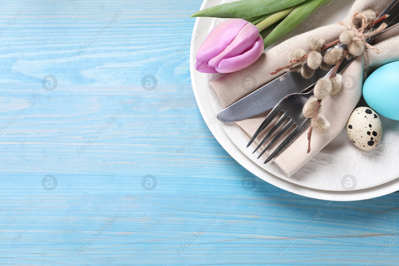 Photo of Festive Easter table setting with eggs and floral decor on light blue wooden background, top view. Space for text