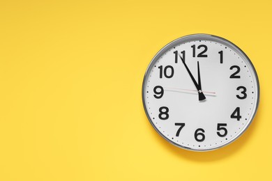 Photo of Clock showing five minutes until midnight on yellow background, top view with space for text. New Year countdown