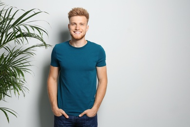 Young man wearing blank t-shirt on light background. Mockup for design