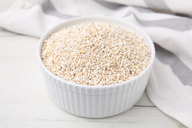 Photo of Dry barley groats in bowl on white wooden table, closeup