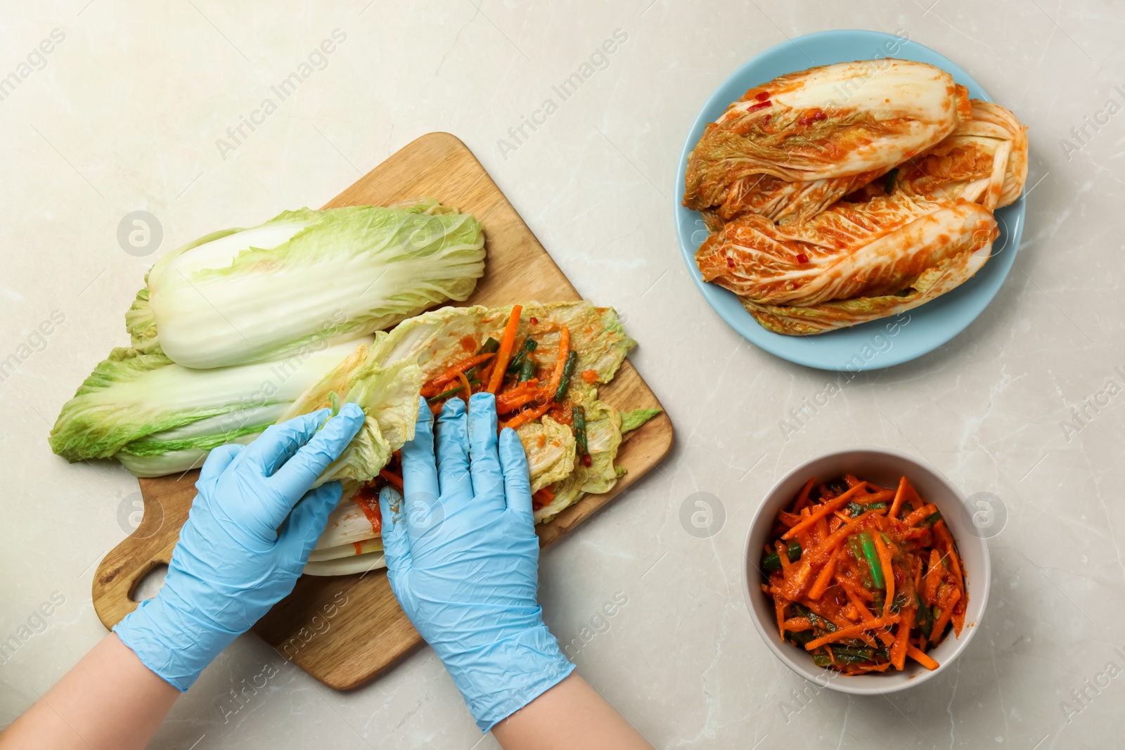 Photo of Woman preparing spicy cabbage kimchi at beige marble table, top view