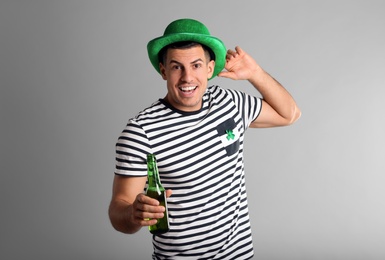 Happy man in St Patrick's Day outfit with beer on light grey background