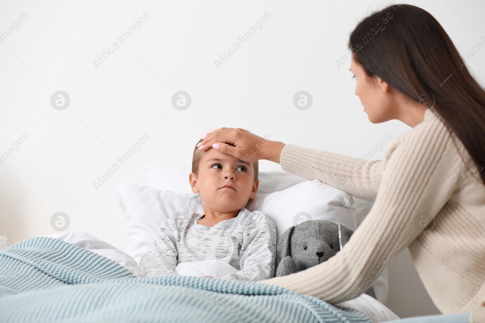 Photo of Mother taking care of her little son suffering from cold in bed, space for text