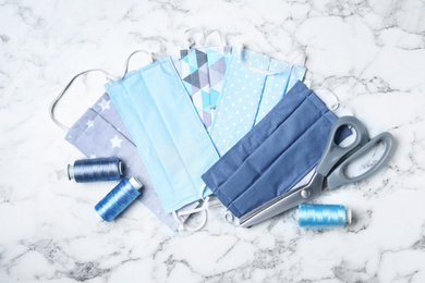 Photo of Homemade protective masks and sewing accessories on white marble background, flat lay