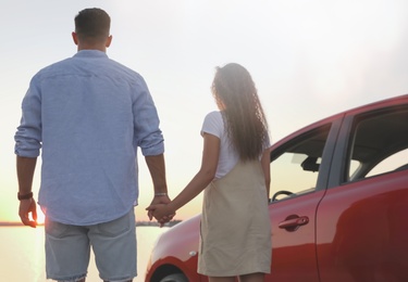 Couple near car outdoors at sunset, back view. Summer trip