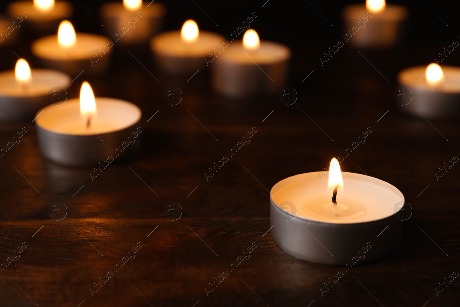 Photo of Wax candles burning on table in darkness, closeup