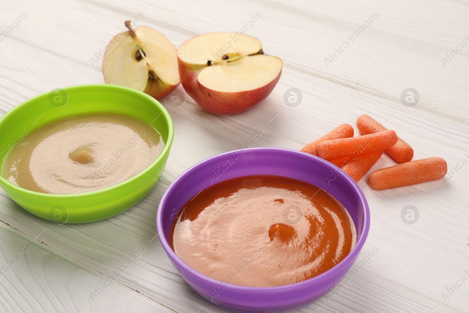 Photo of Baby food. Purees of apples and carrots in bowls on white wooden table