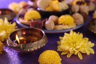 Photo of Diwali celebration. Diya lamp and chrysanthemum flowers on shiny violet table, closeup