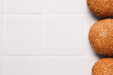 Fresh buns with sesame seeds on white tiled table, flat lay. Space for text