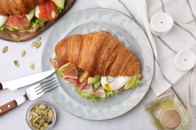 Photo of Delicious croissant with prosciutto, avocado and egg served on white table, flat lay