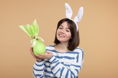 Photo of Easter celebration. Happy woman with bunny ears and wrapped egg on beige background