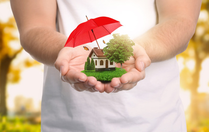 Image of Insurance concept - umbrella demonstrating protection. Man holding house model with green lawn, closeup