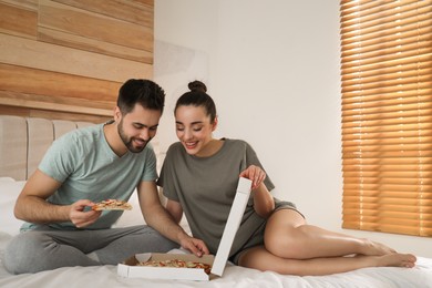 Happy couple in pajamas eating pizza on bed at home