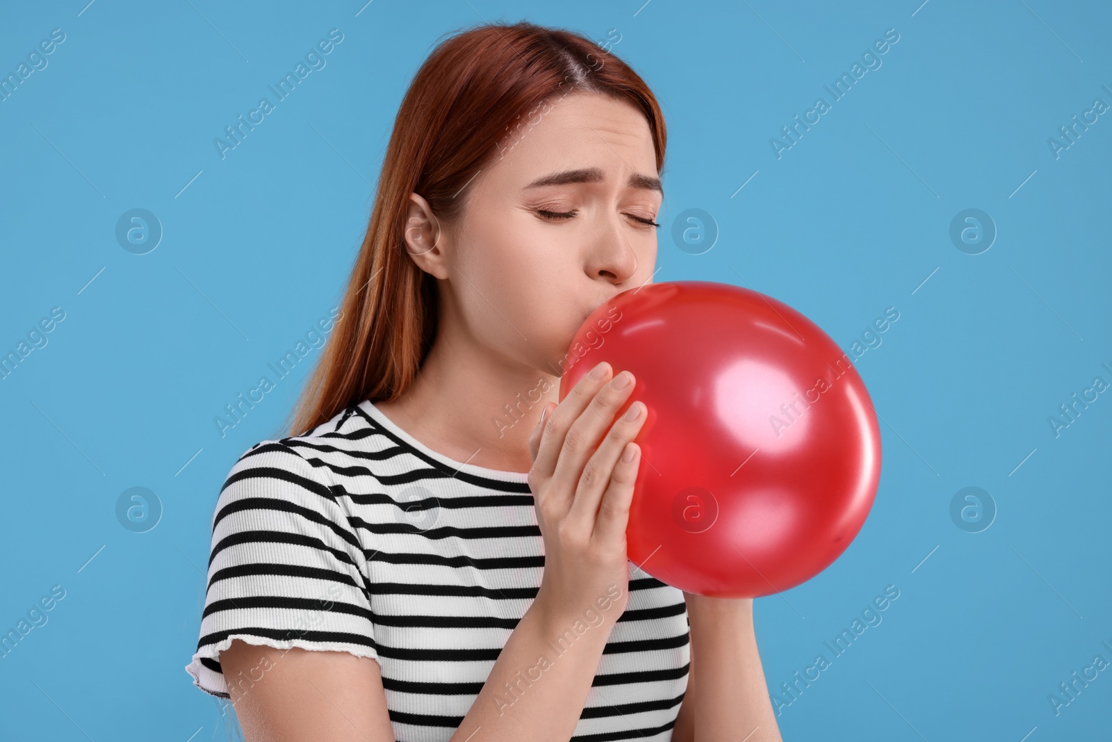 Photo of Woman inflating red balloon on light blue background