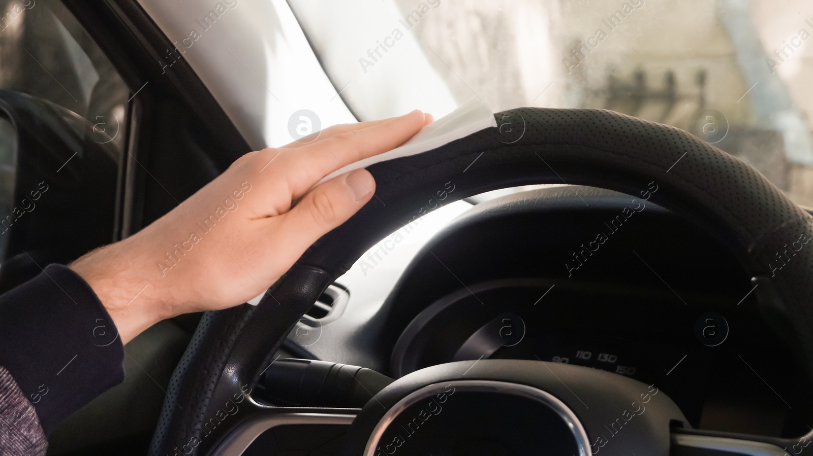 Photo of Man cleaning steering wheel with wet wipe in car, closeup. Protective measures