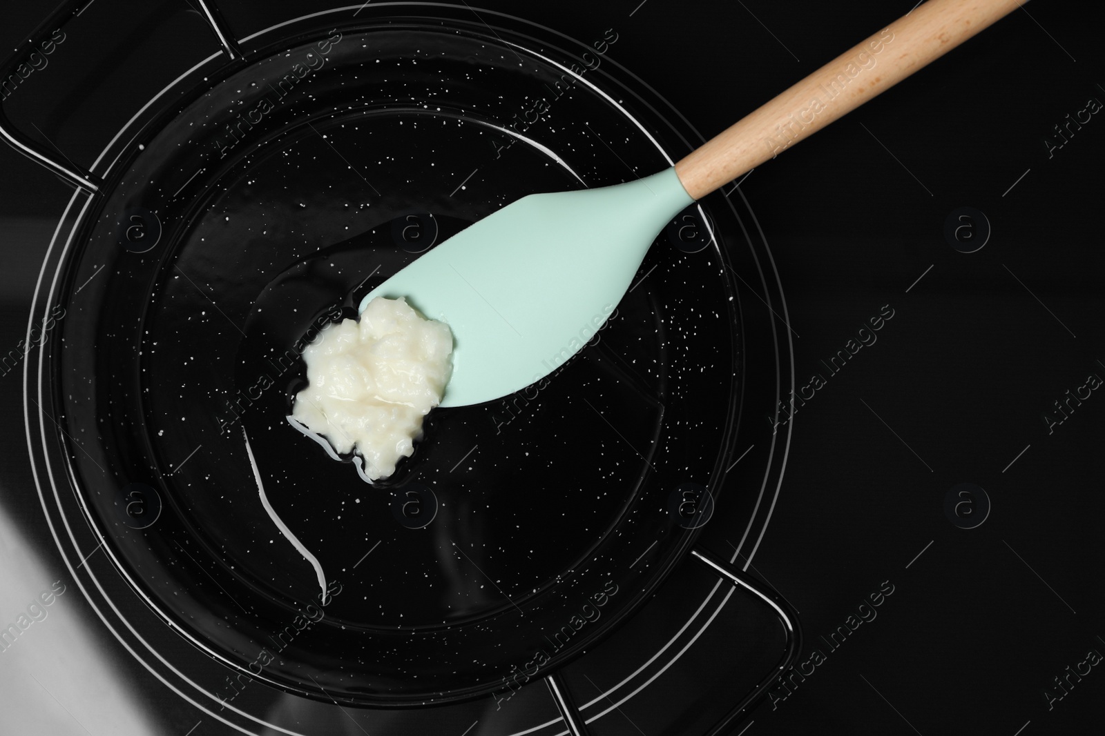 Photo of Frying pan with coconut oil and spatula on induction stove, top view. Healthy cooking