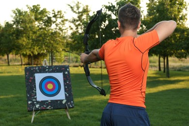 Man with bow and arrow aiming at archery target in park, back view