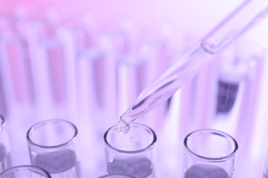 Photo of Dripping liquid from pipette into test tube on violet background, closeup