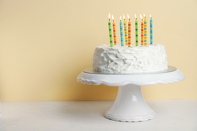 Birthday cake with candles on table against color background