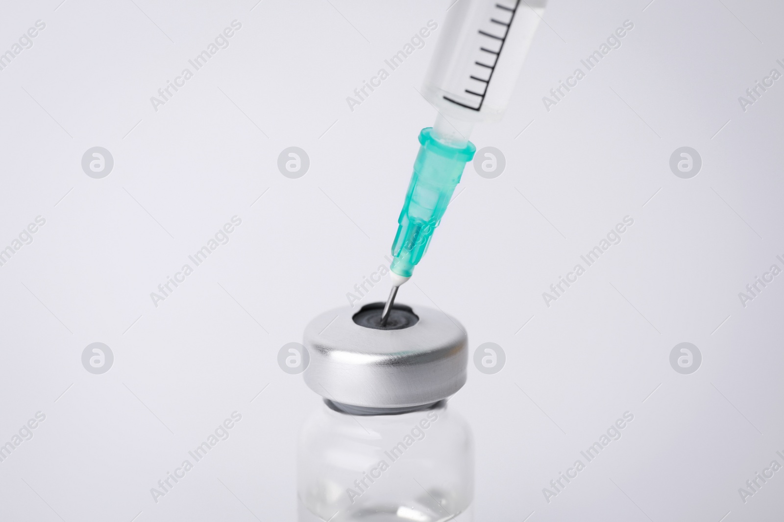 Photo of Filling disposable syringe with medicine from vial on white background, closeup