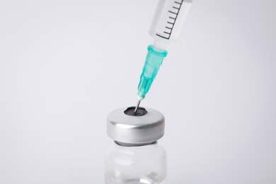 Filling disposable syringe with medicine from vial on white background, closeup