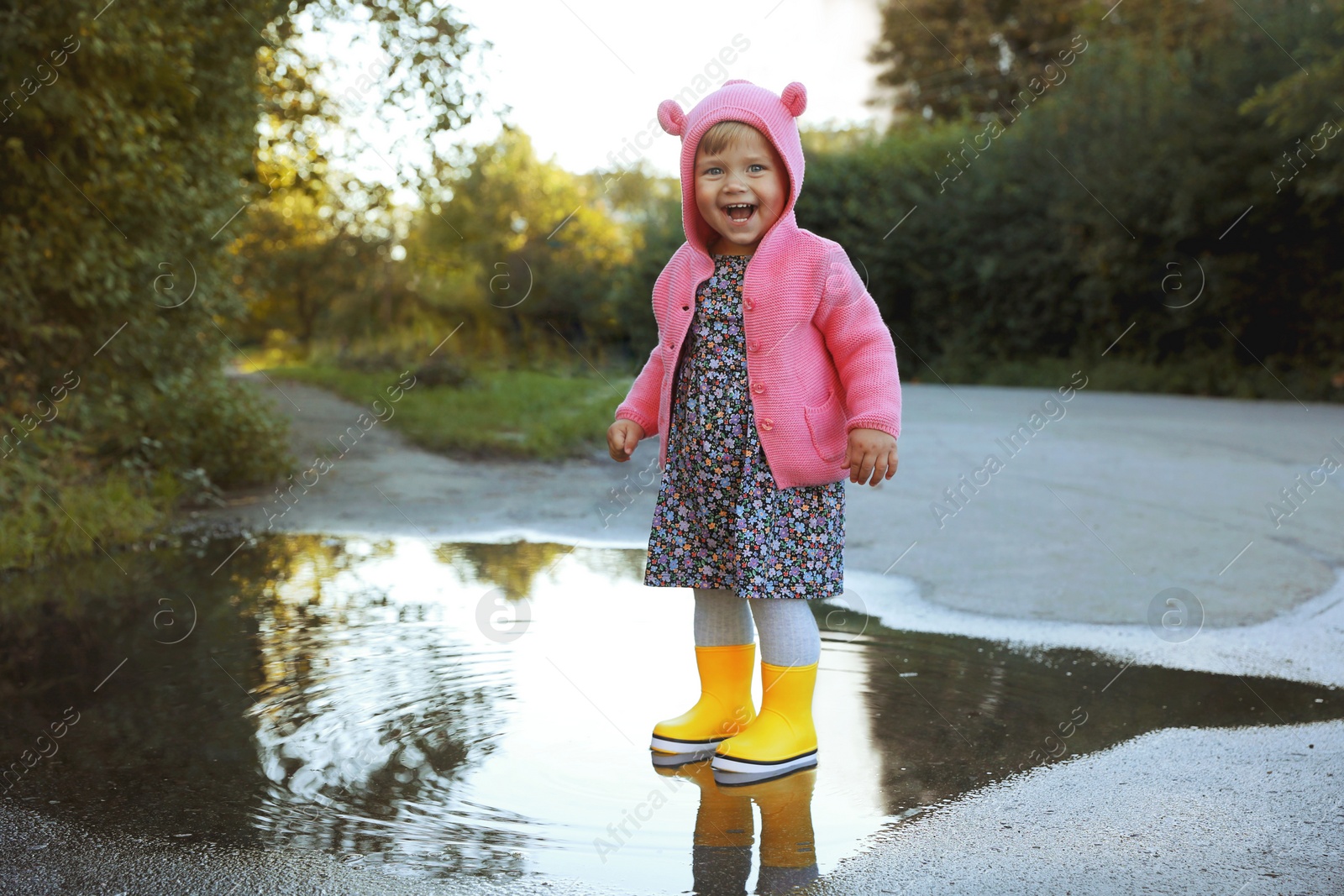 Photo of Little girl wearing rubber boots standing in puddle outdoors. Autumn walk