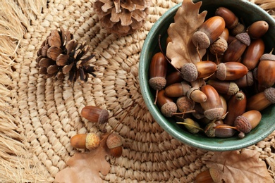 Photo of Acorns, oak leaves and pine cones on wicker mat, flat lay