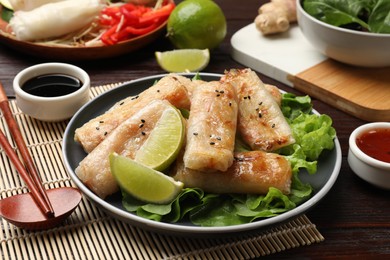 Photo of Tasty fried spring rolls, lettuce and sauce on wooden table, closeup