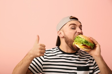 Photo of Young man eating tasty burger on color background. Space for text