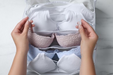 Photo of Woman putting bra into organizer with underwear at white marble table, top view