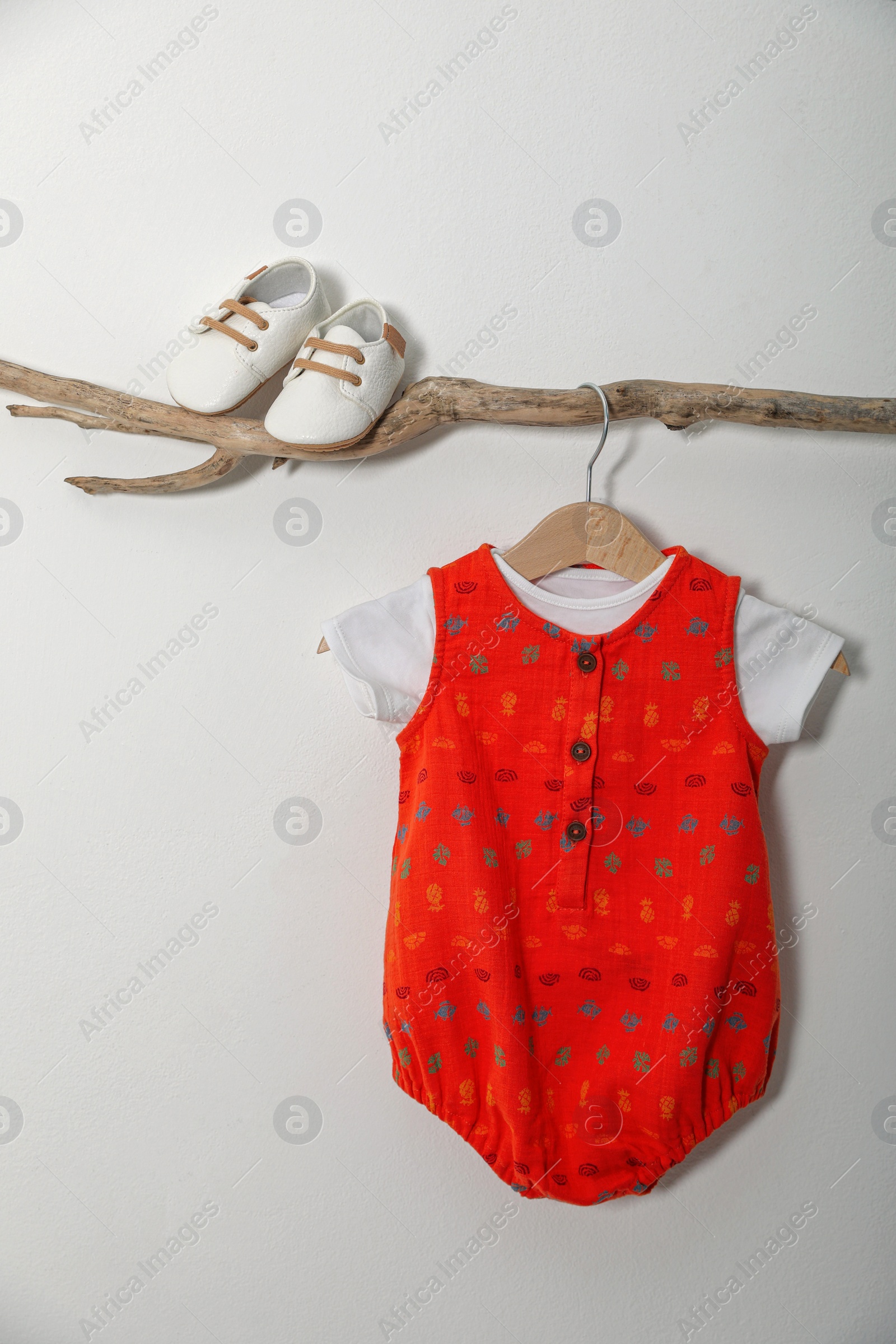 Photo of Baby bodysuit and booties on decorative branch near light grey wall